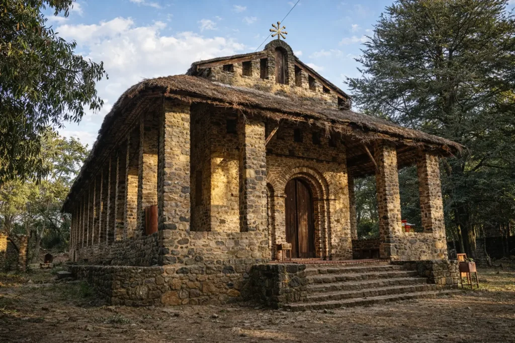 exterior view of Debre Birhan Selassie Church in Gondar, Ethiopia, featuring its stone columns, thatched roof, and traditional Ethiopian Orthodox architecture surrounded by trees
