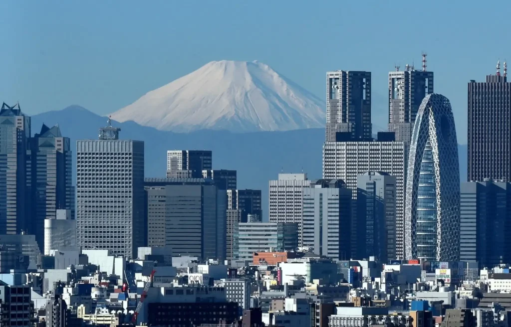 Japan's highest mountain, Mount Fuji is seen behind the skyline of the Shinjuku area of Tokyo